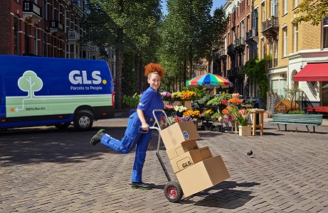 Fröhliche GLS Fahrerin schiebt eine Sackkarre mit Paketen durch die Innenstadt