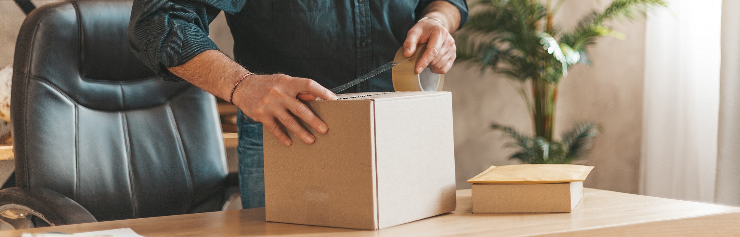 Send a parcel. Mature man packing cardboard box in the office. Delivery of postal cargo.