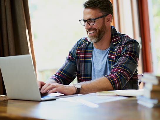 Ein Mann der lachend vor einem Laptop sitzt