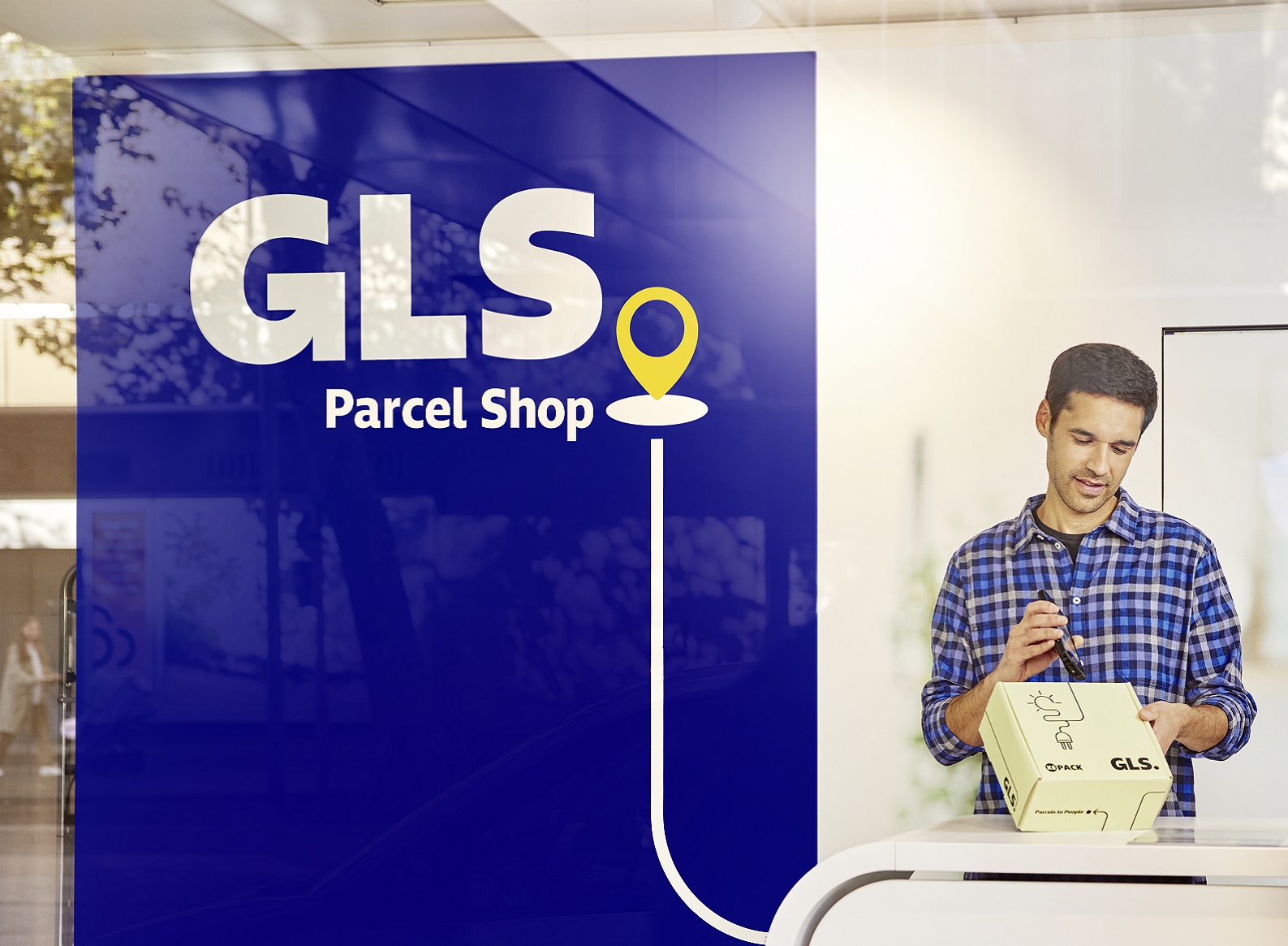 Ein GLS PaketShop-Betreiber steht in seinem Shop am Tresen und versendet ein Päckchen