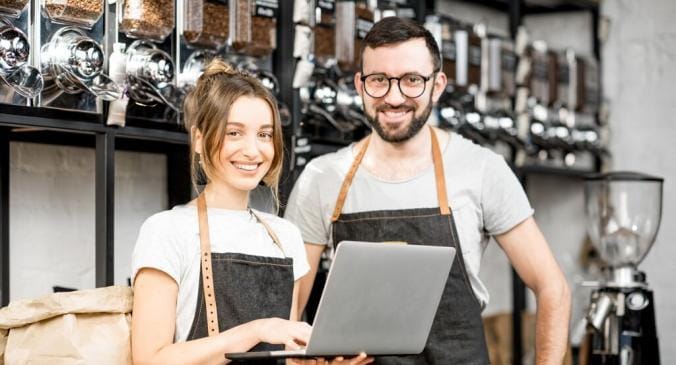 Mann und Frau stehen mit einem Laptop in der Hand in ihrem Geschäft und verkaufen Kaffeemaschinen
