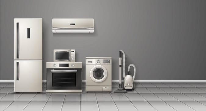 Verchromter, moderner Kühlschrank, Microwelle, Waschmaschine und Staubsauger stehen aufgereit vor einer Wand