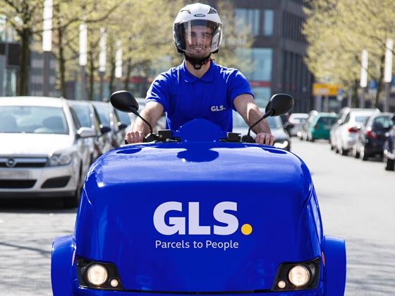 Ein junger GLS-Mitarbeiter trägt zwei Pakete in eine Filiale