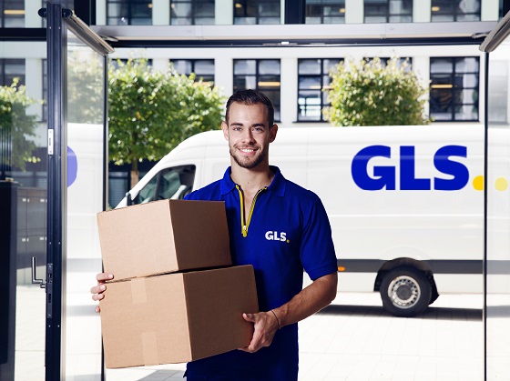 Ein junger GLS-Mitarbeiter trägt zwei Pakete in eine Filiale