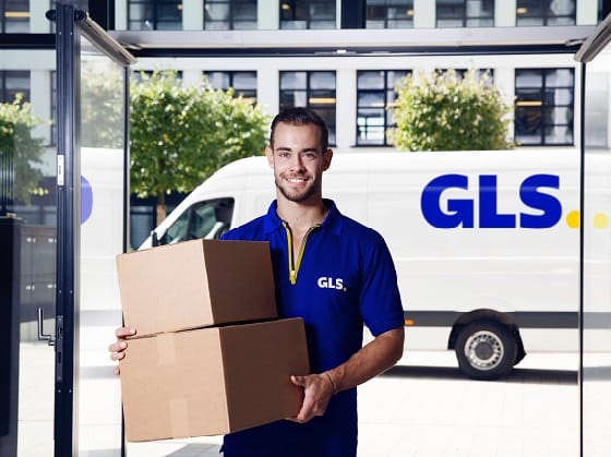 A young GLS employee carries two packages into a branch office